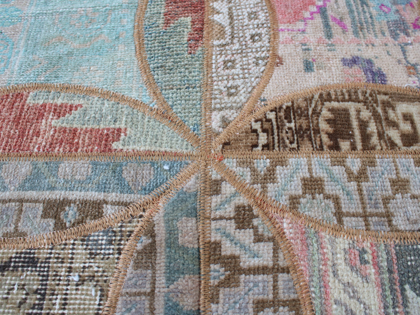 Close-up of a woven rug or textile with a geometric starburst pattern in muted pastel tones including beige, blue, pink, brown, and cream.