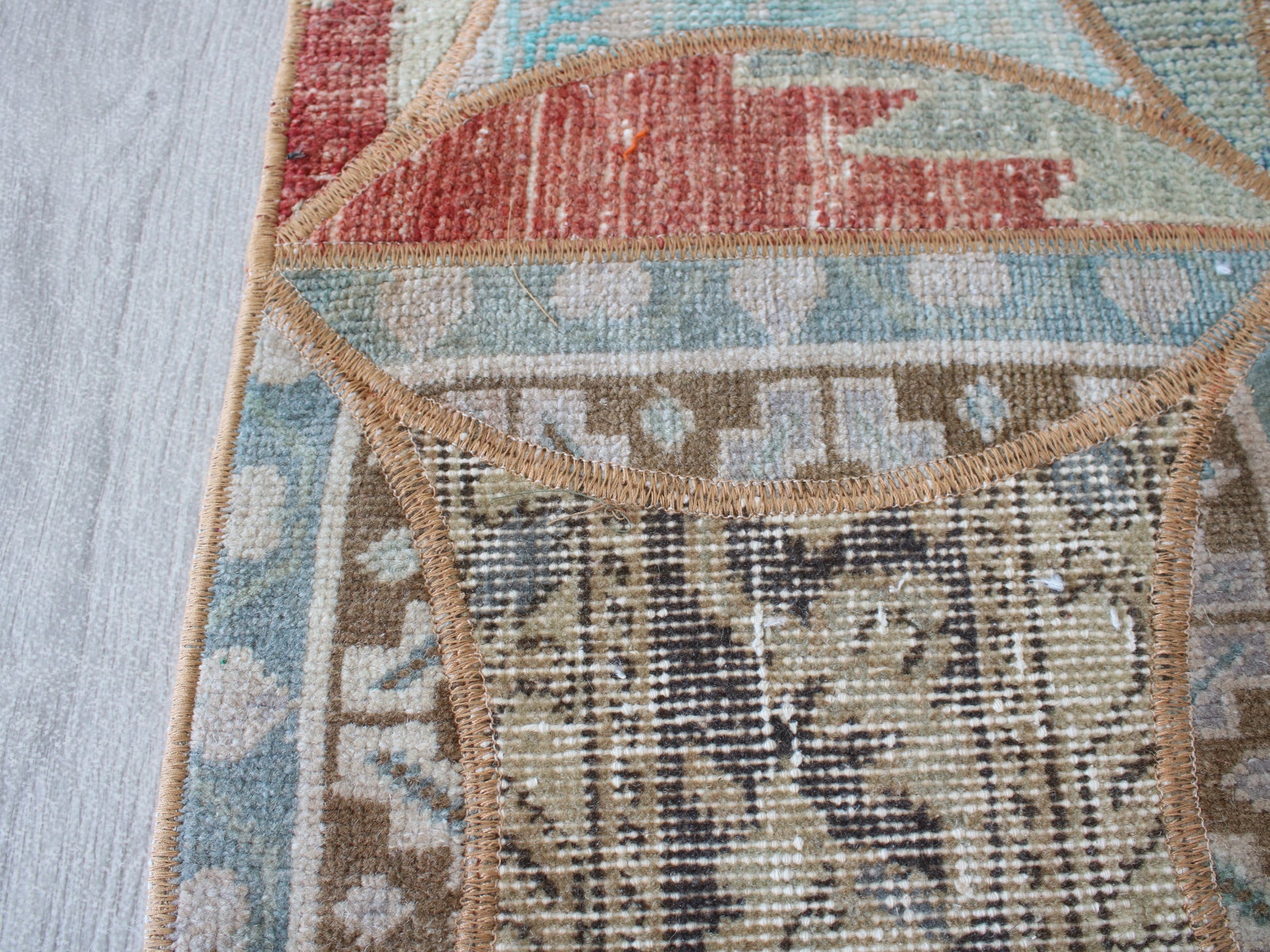 Close-up detail of a patterned area rug showing woven sections in beige, brown, light blue, and muted red, with a tan stitched border on a light wood floor.