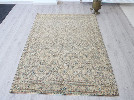 A rectangular vintage-style area rug with a beige base and blue-gray floral pattern, laid out on a light gray wood floor.