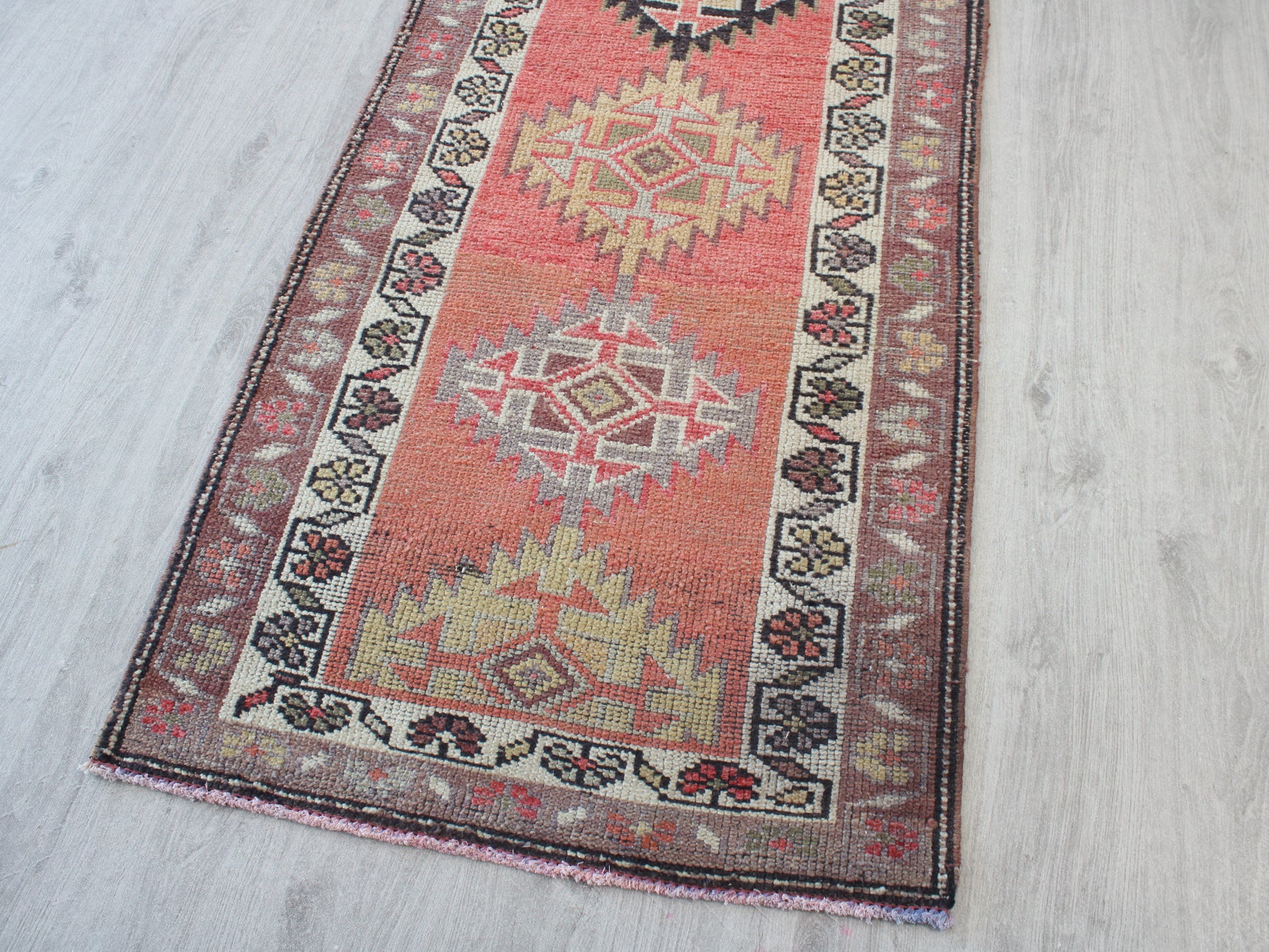 A traditional Persian-style runner rug with geometric diamond motifs, displayed diagonally on a light gray wood floor.
