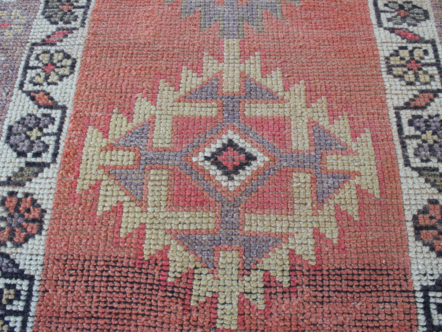 A close-up of a woven rug with a central geometric medallion pattern in muted coral red, beige, gray, and black.
