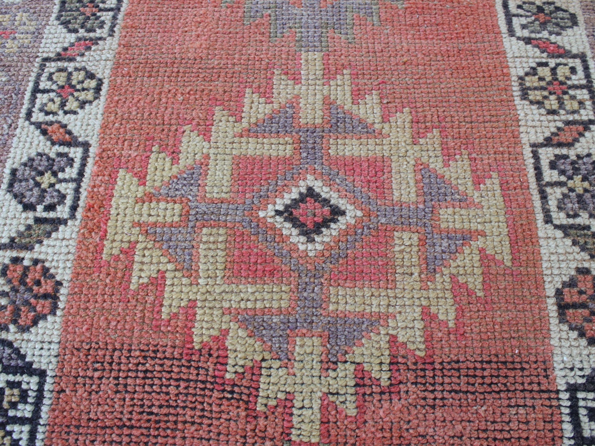 A close-up of a woven rug with a central geometric medallion pattern in muted coral red, beige, gray, and black.