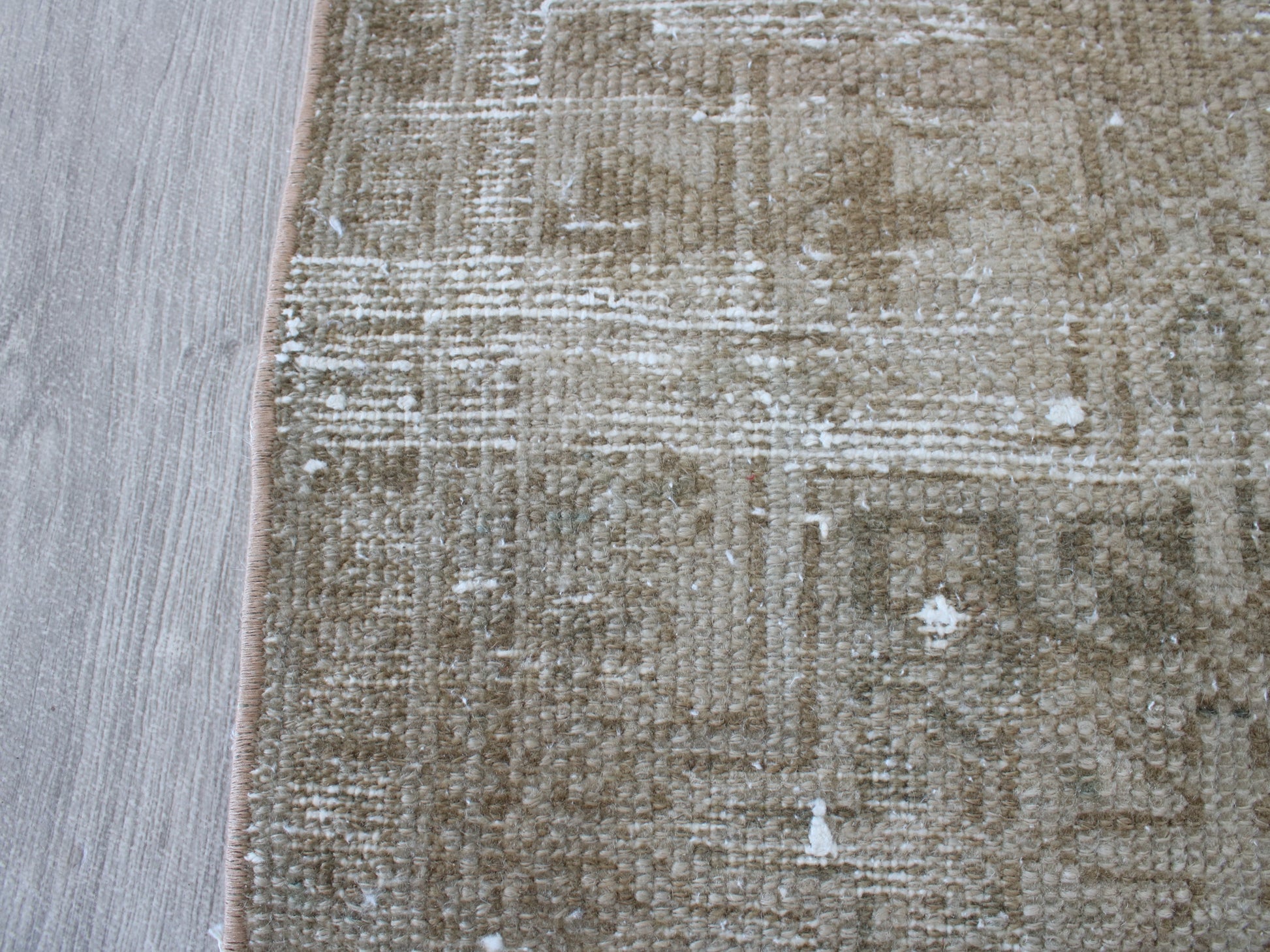 A close-up of a distressed area rug with a beige and brown geometric pattern, shown next to a light gray wood floor.