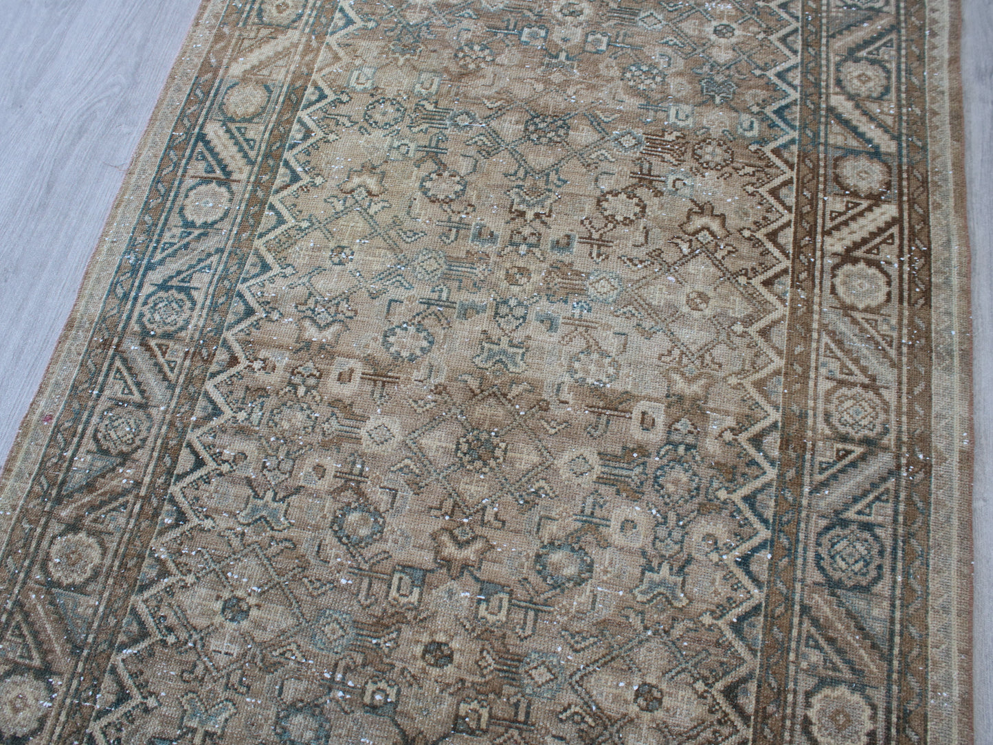 A traditional oriental-style area rug with an intricate floral and geometric pattern in beige, brown, and muted blue, laid out on a light gray floor.