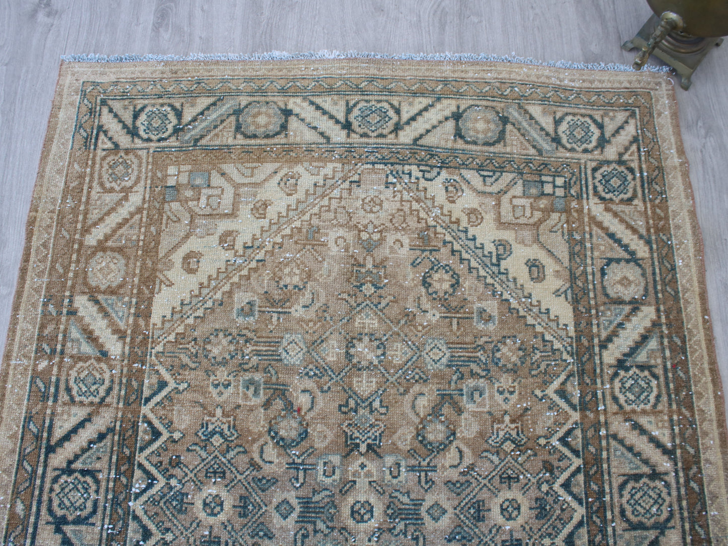 A traditional oriental-style area rug with a beige, brown, and blue geometric pattern, laid out on a light gray wood floor.
