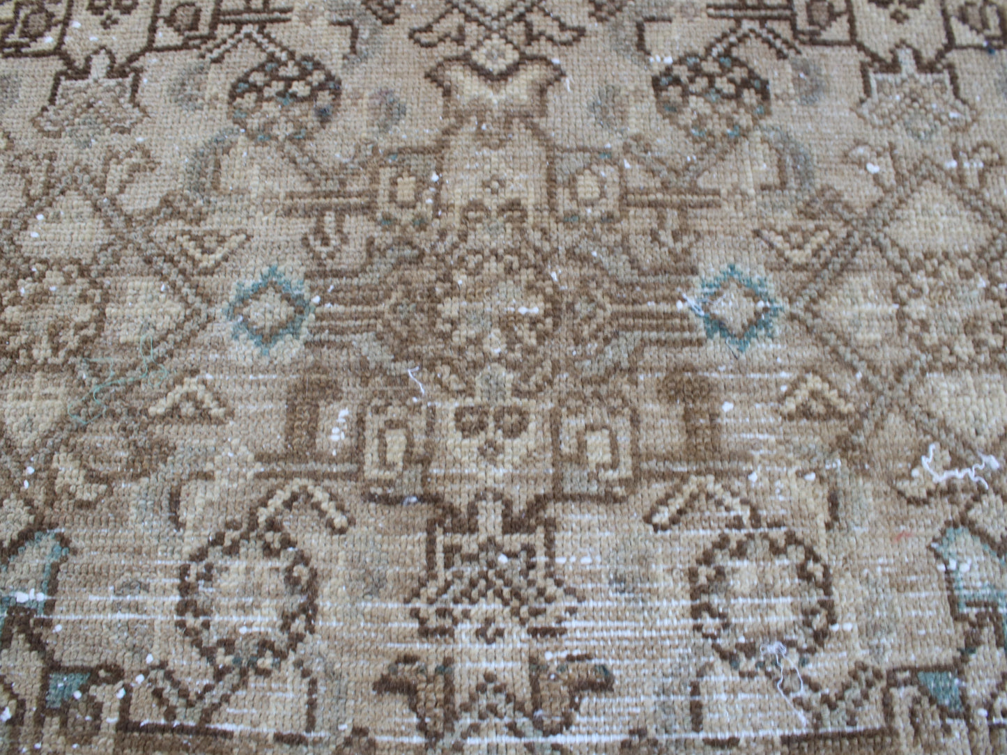 A close-up of a vintage-style woven rug featuring a traditional geometric pattern in shades of brown, beige, and light blue.