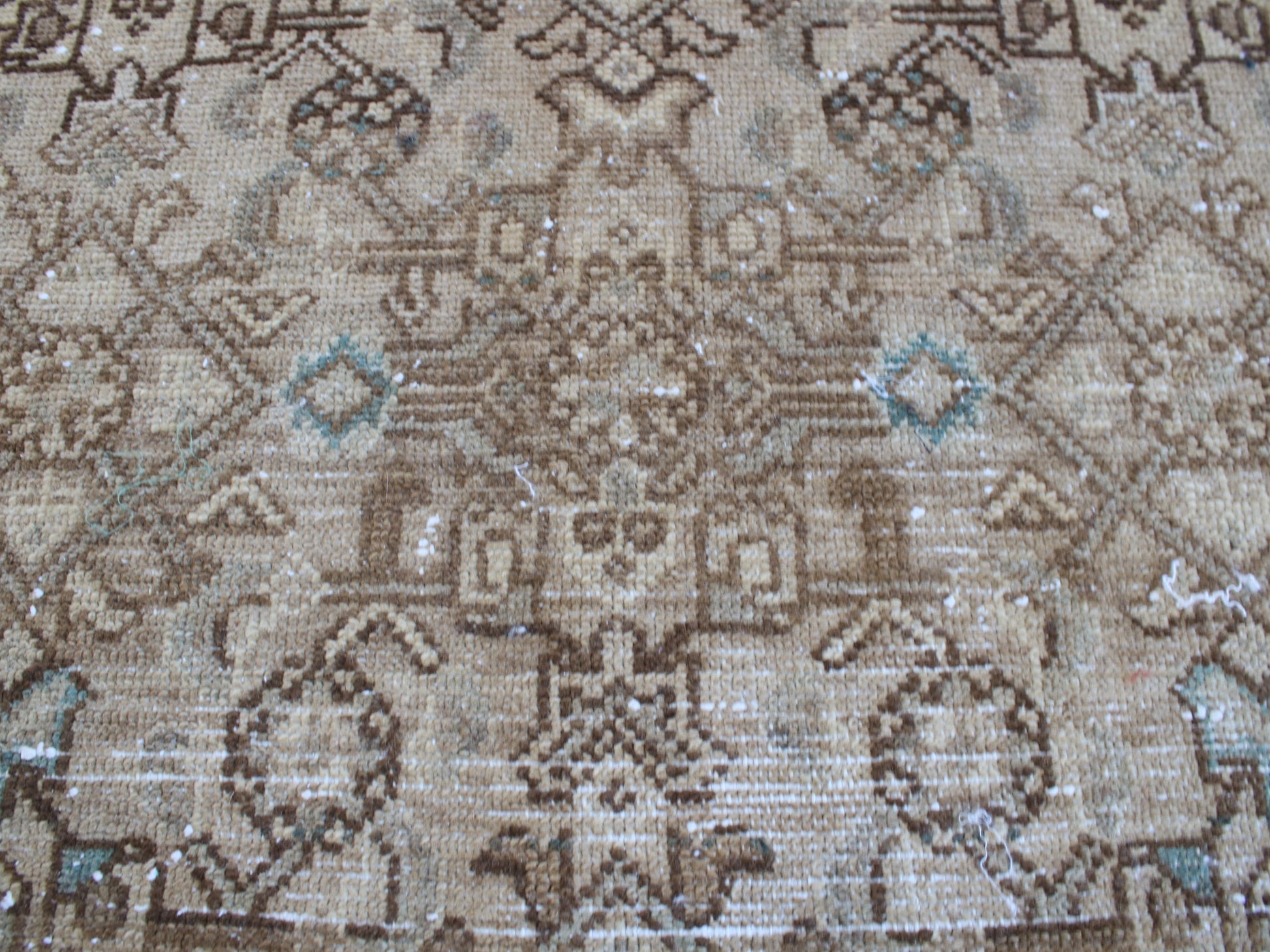 A close-up of a vintage-style woven rug featuring a traditional geometric pattern in shades of brown, beige, and light blue.