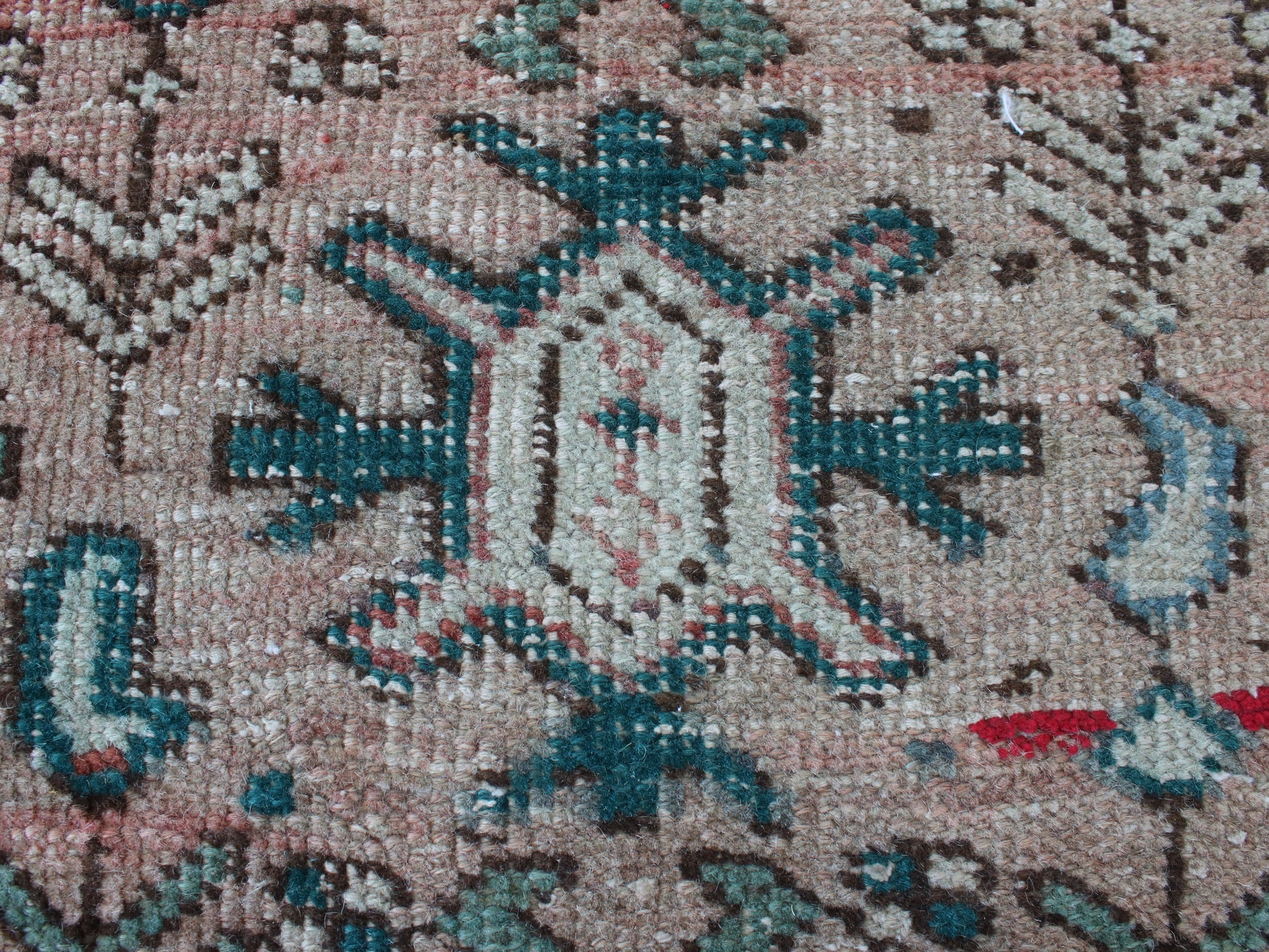 Close-up of a woven rug or textile with a central medallion motif in beige, teal blue, brown, and small red accents.