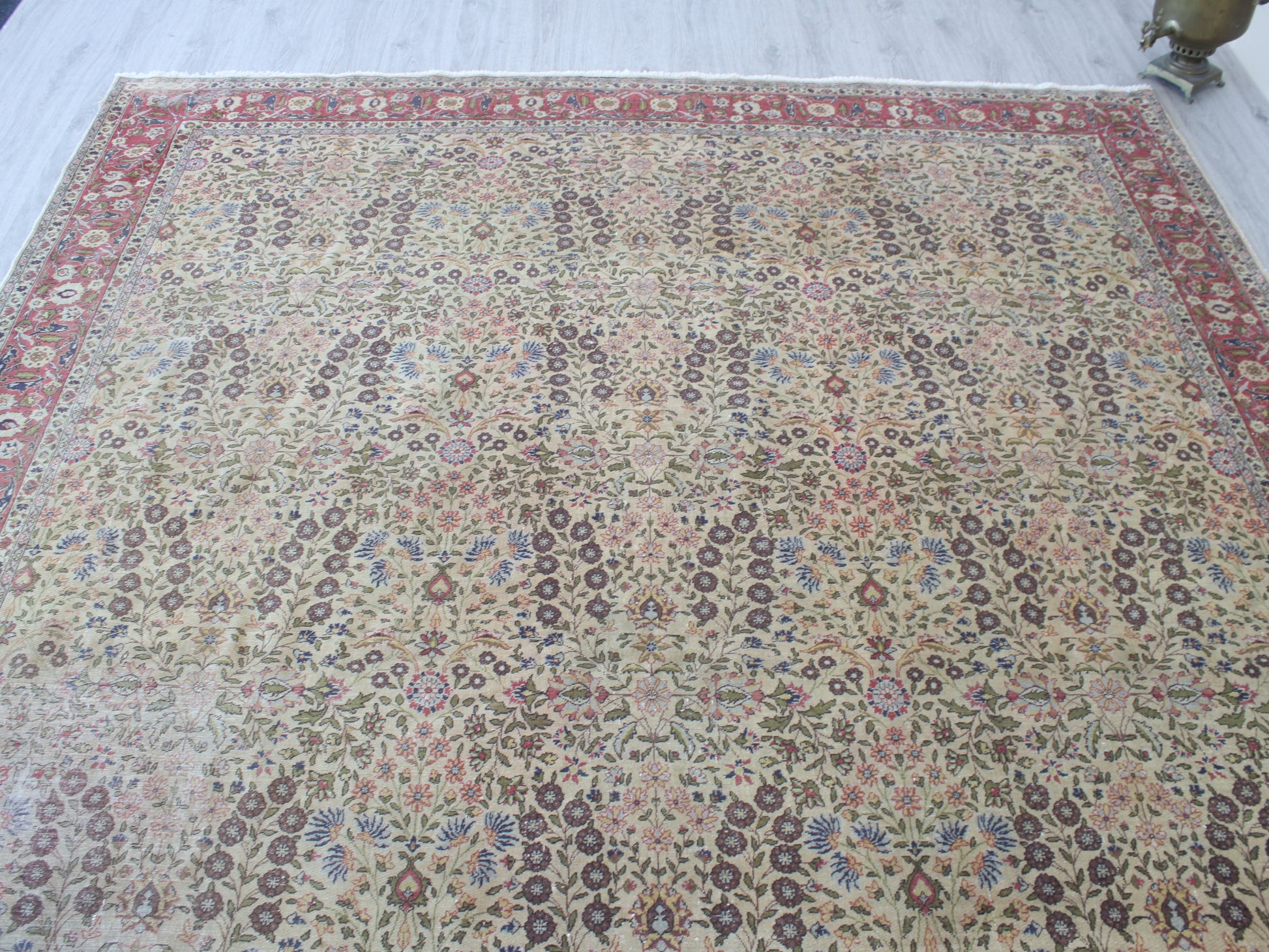 A large traditional oriental area rug with an intricate floral pattern, featuring a beige center field, red borders, and multicolored details, laid out on a light-colored floor.