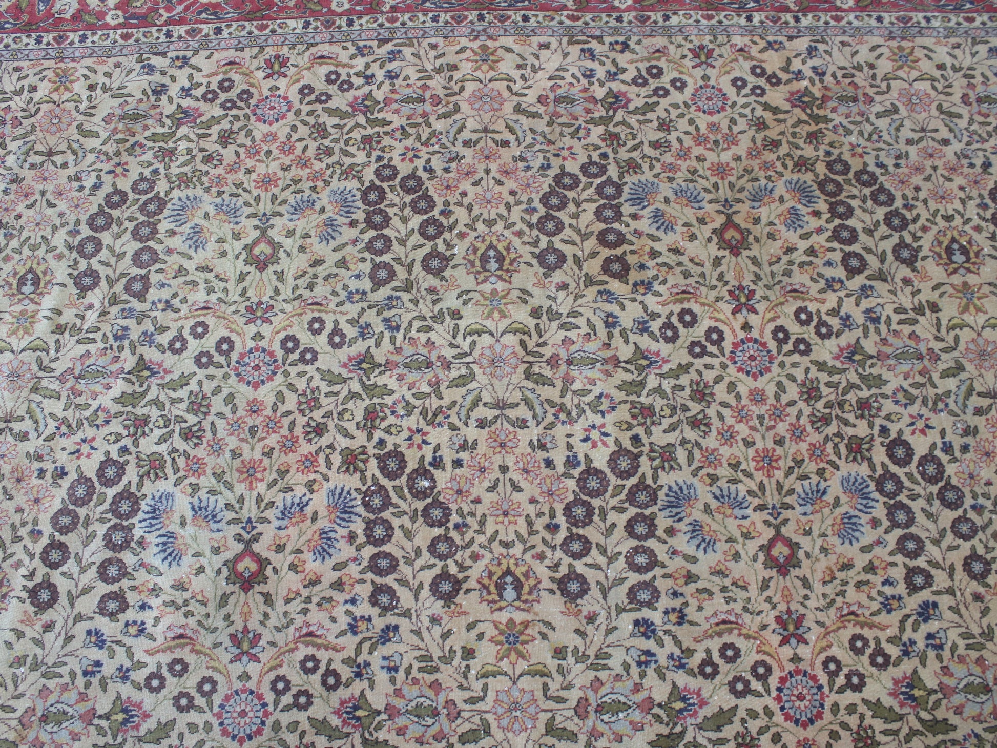 An intricate traditional Persian-style area rug with a dense floral and vine pattern on a beige background, featuring accents of blue, pink, green, and brown.