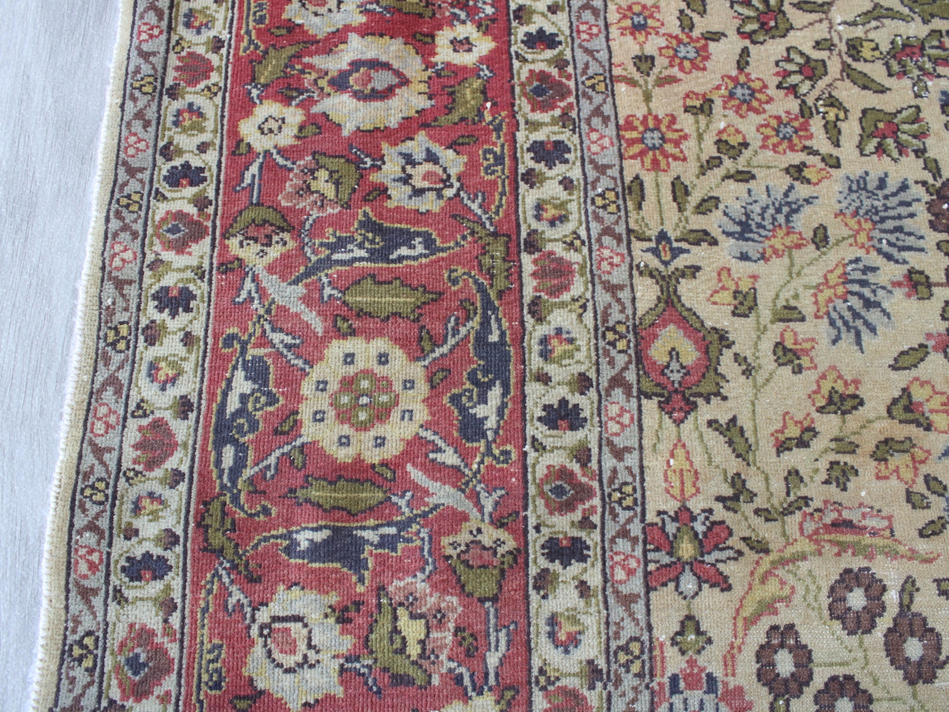 Close-up of an ornate patterned area rug showing a red central field with floral motifs, cream and beige sections, and blue, green, and rust accents in the woven design.