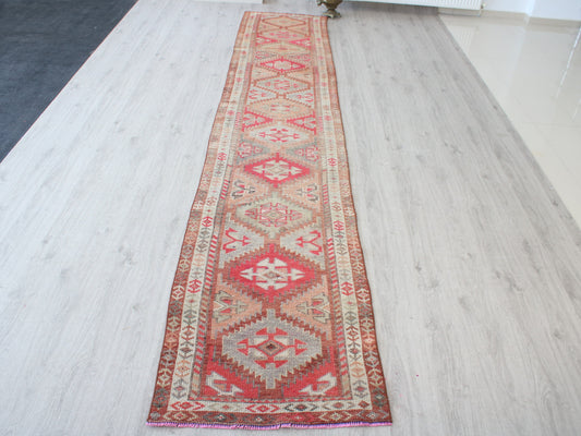 A long rectangular area rug with a traditional geometric pattern in red, beige, and brown, laid out on a light-colored wood floor.