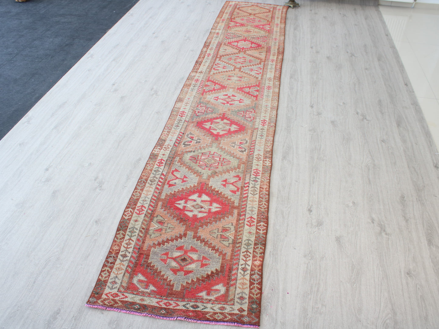 A long rectangular area rug with a traditional geometric kilim pattern in red, beige, and brown, laid out on a light-colored wood floor.