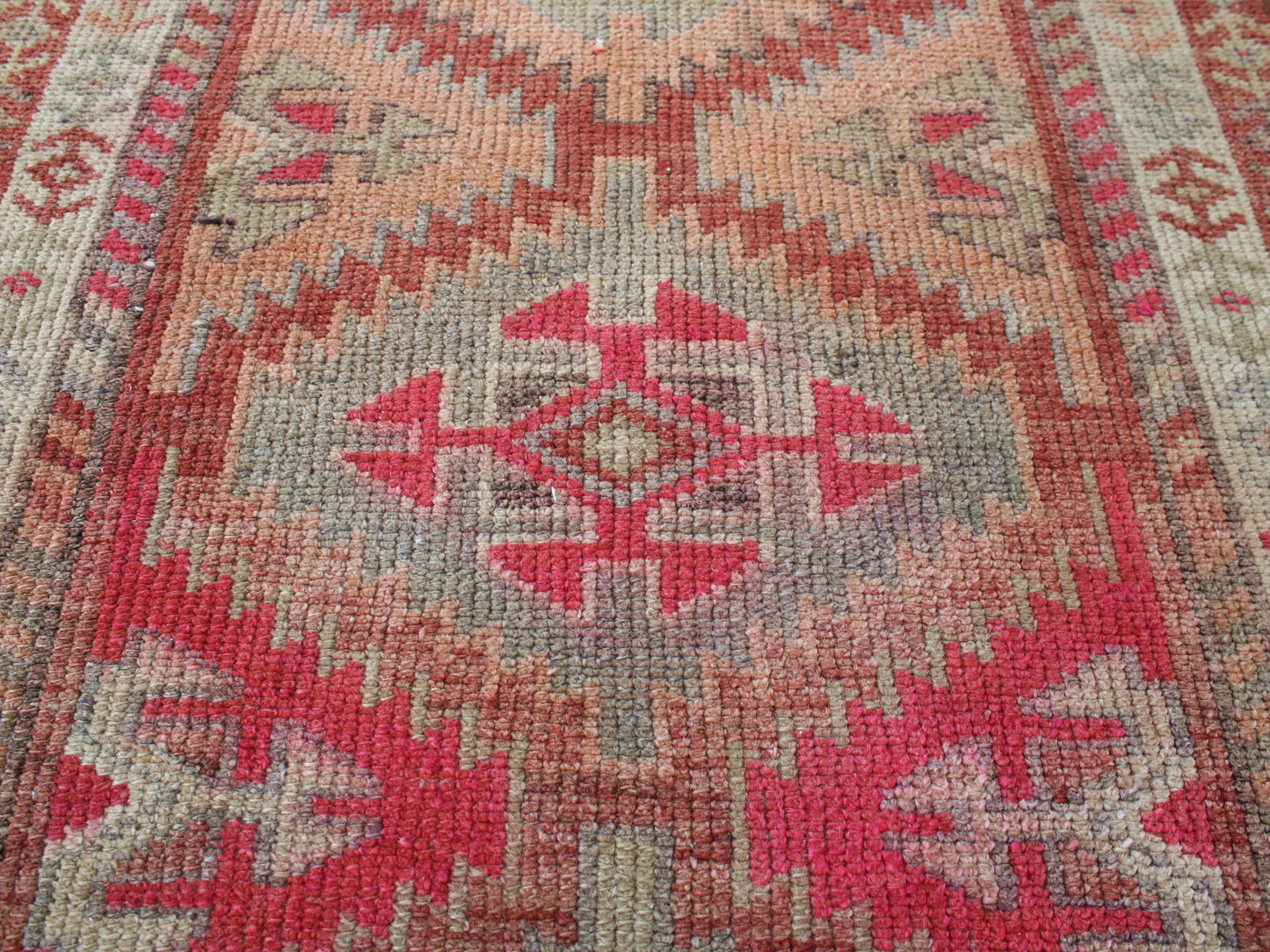 A close-up of a woven rug with a geometric tribal pattern in red, pink, beige, and gray.