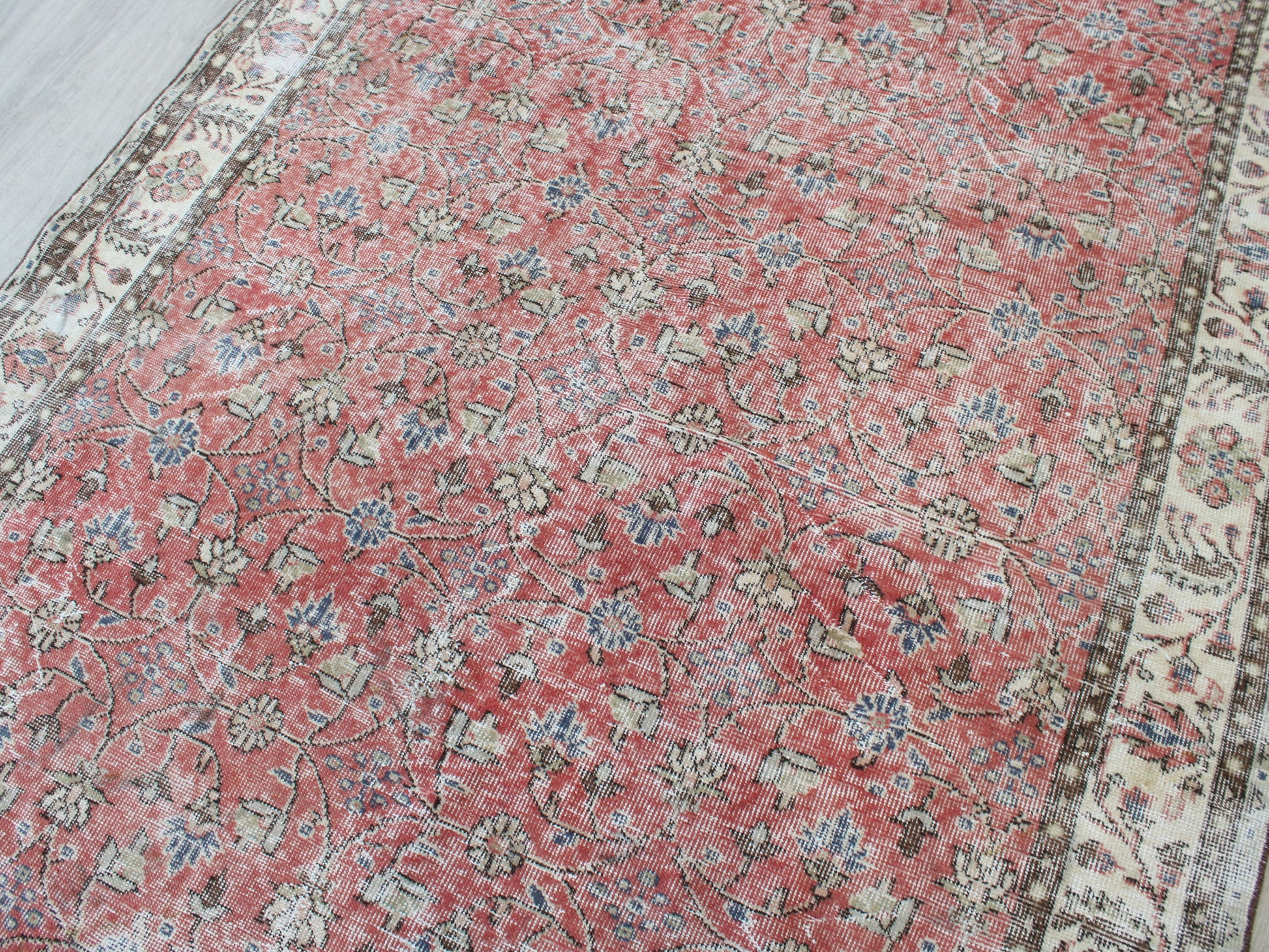 A traditional Persian-style area rug with a dusty red field, cream borders, and blue and beige floral motifs.