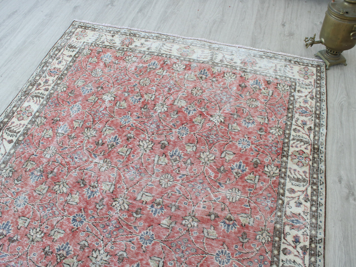 A rectangular vintage-style Persian-style area rug with a faded red center, cream borders, and blue floral motifs, laid out on a light gray wood floor.