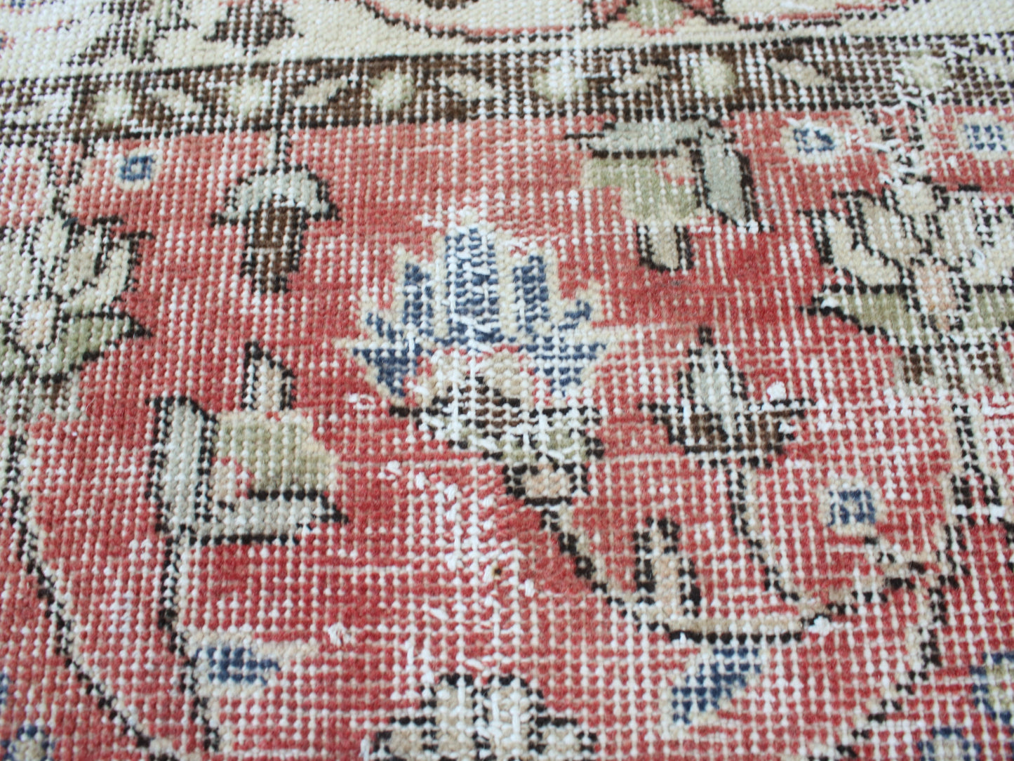 A close-up of a patterned rug showing a coral red field with beige, blue, and brown floral motifs.